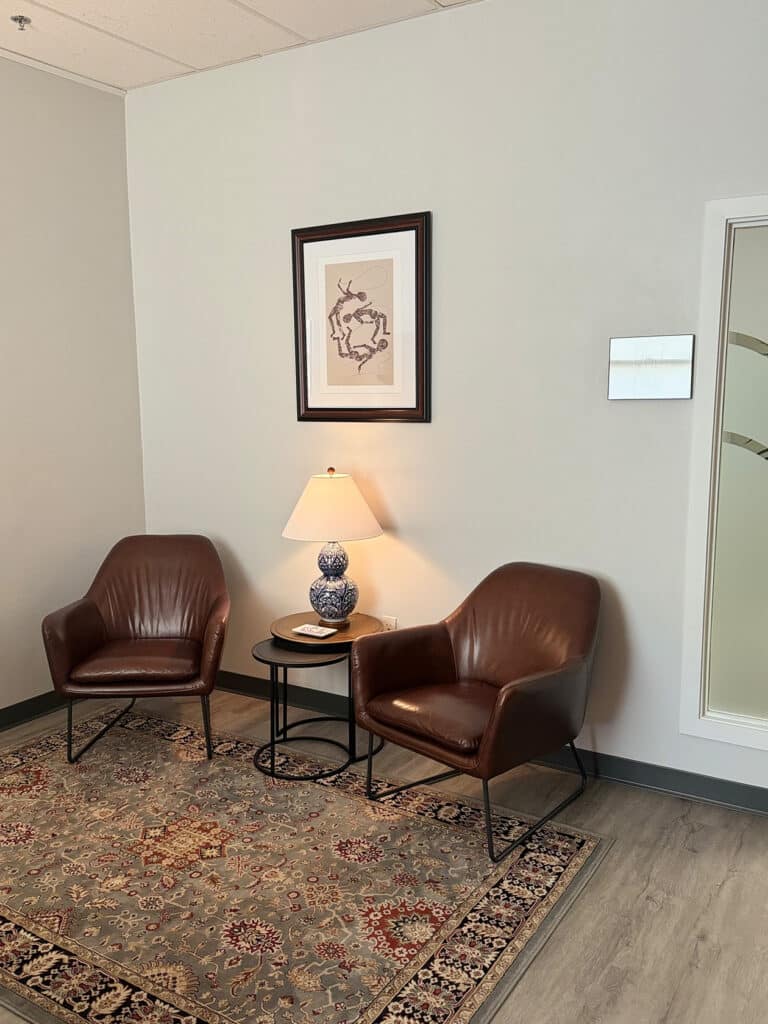 Two brown leather armchairs either side of a small table and lamp, on a patterned rug in a waiting area at Massachusetts Center for Addiction