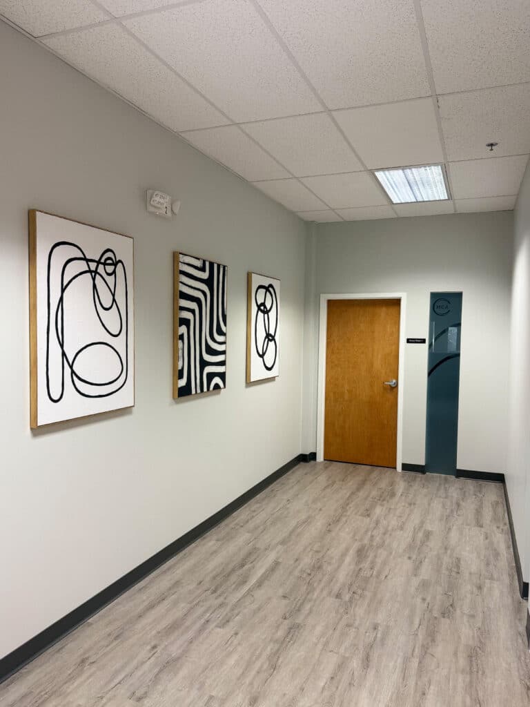 Hallway hung with framed abstract artwork leading to a group therapy room at Massachusetts Center for Addiction