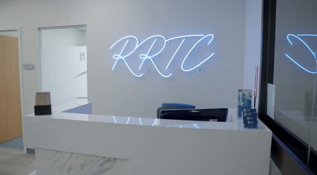 Reception desk at Rockland Recovery Treatment Center in Braintree, with the letters RRTC in blue neon script on the wall behind
