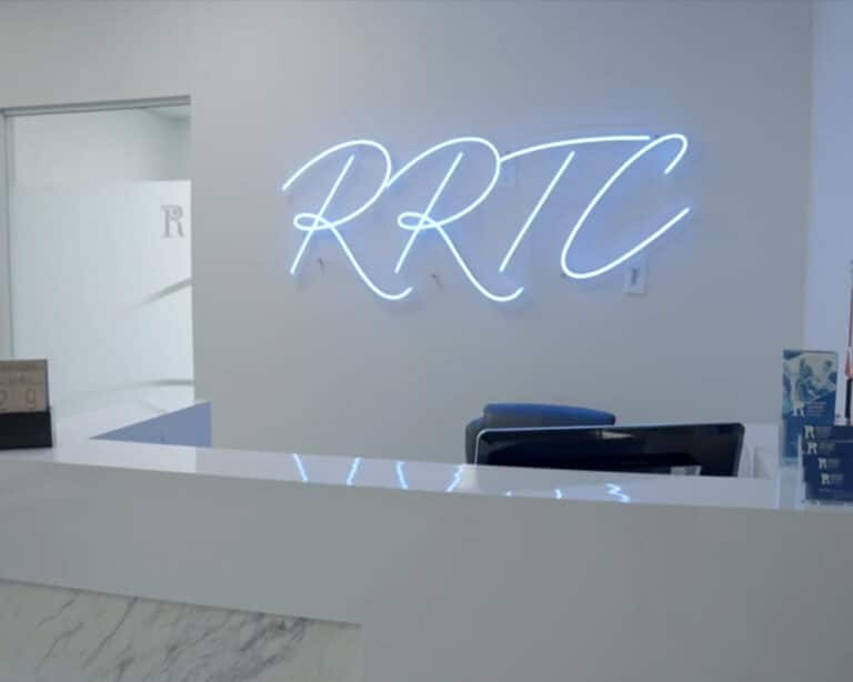 Reception desk at Rockland Recovery Treatment Center, with the RRTC initials lit in blue neon on the wall behind it