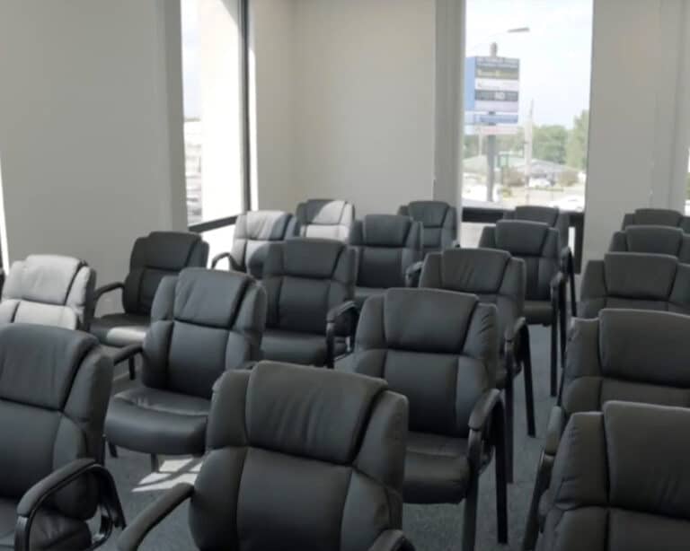 Group therapy room set with rows of grey armchairs facing the front, daylight through corner windows