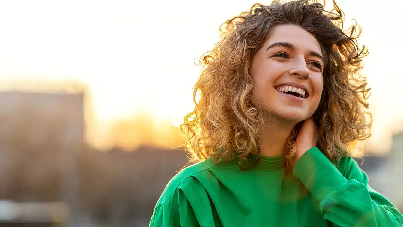 a woman in a green shirt smiling outside with building in the background symbolizing happiness after relapse prevention in addiction recovery