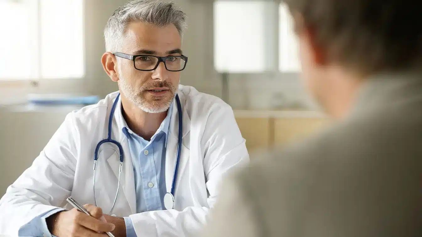 a doctor with a stethoscope around his neck sitting with a male patient reviewing what to expect during drug addiction treatment