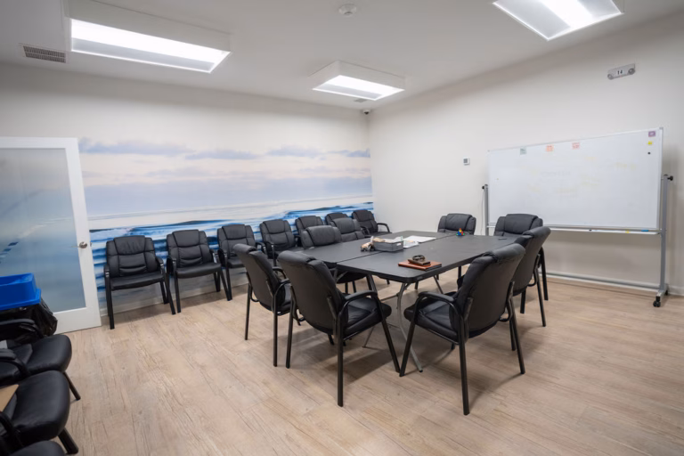 Group therapy room with a central table, black chairs along the wall, a whiteboard and a mural of an ocean shoreline running the length of one wall